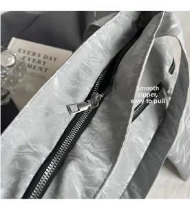 Detail showing smooth black metal zipper closure on silver pleated leather tote bag
