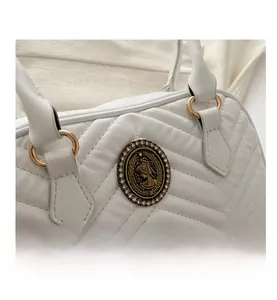 Close-up of white quilted crossbody bag with vintage rhinestone crest and gold hardware