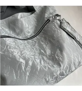 Detail of silver metallic tote bag with wrinkled texture, black zipper, and small coin purse