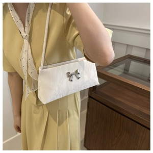 Detailed close-up of white pleated texture and silver bow buckle on small shoulder bag