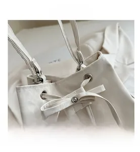 Close-up of cream white bucket bag featuring silver eyelets and drawstring bow detail