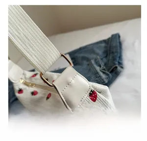 Detail of white corduroy bag showing strawberry embroidery and metallic ring connection