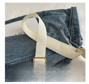 Close-up of white woven shoulder strap with light gold metal buckle on denim