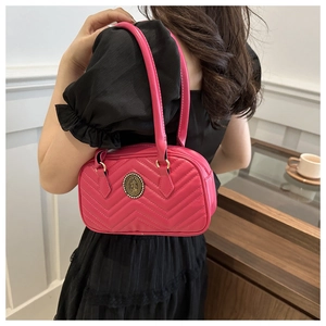 Close-up of rose red V-quilted shoulder bag with round vintage emblem on model