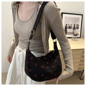Detail view of black corduroy shoulder bag with red strawberry pattern on a female model