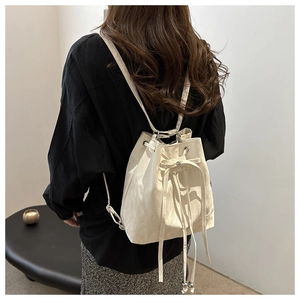 Rear view of model wearing a beige drawstring bucket bag with decorative ribbons