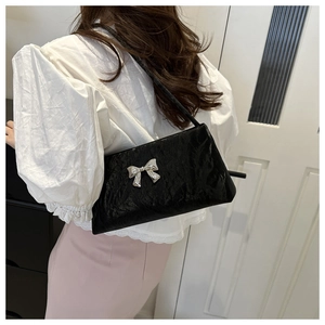 Détail d'un sac à bandoulière plissé noir avec un nœud argenté porté par un mannequin