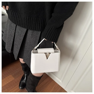 Detail of white lychee leather handbag featuring prominent golden V-shaped metal clasp