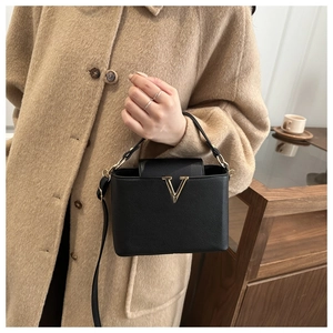 Close-up of black litchi pattern handbag featuring a gold V-shaped metal logo buckle