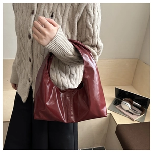Close-up of a burgundy patent leather underarm bag held by a model in a beige knit sweater
