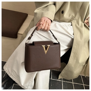 Detail of dark brown pebble leather handbag with gold V-shaped metal buckle and top handle