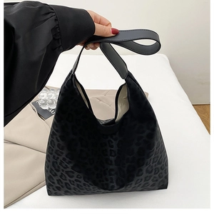 Detail of dark leopard print tote bag with black leather handle on neutral background