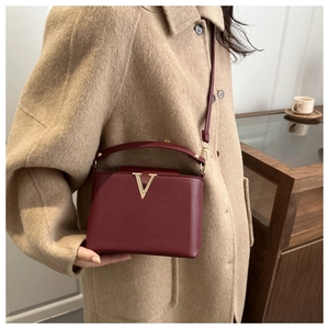 Sac à main bordeaux en cuir grainé avec logo V doré porté sur un manteau en laine