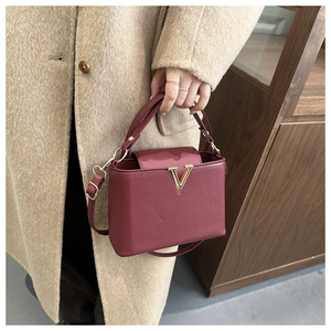 Dettaglio della borsa in pelle bordeaux con fibbia a V dorata su un cappotto beige