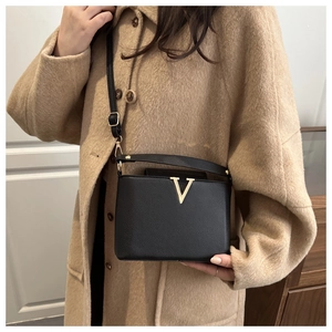 Détail du sac bandoulière noir en cuir grainé avec logo V doré sur un manteau en laine