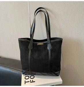Detail of black suede tote bag with leather straps and central fashion logo tag