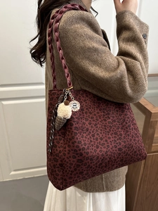 Burgundy leopard print tote bag with woven handles and plush charm on casual coat