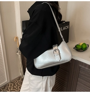 Detail of silver leather underarm bag with metal buckle worn by model in casual setting