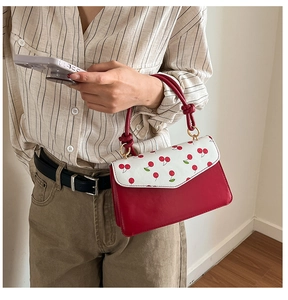 Detail of red cherry print handbag featuring knotted rope handle and gold metal buckles