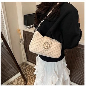 Detailansicht der cremefarbenen Schultertasche mit M-Monogramm und Gold-Logo