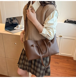 Detail of a large brown pleated tote bag with adjustable strap in an office setting