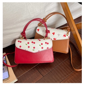 Détail de sacs bandoulière rouges et marron avec motifs cerise et ours dans un cadre chaleureux