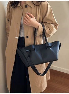 Detail of a black pleated tote bag with side belt accents on a tan trench coat