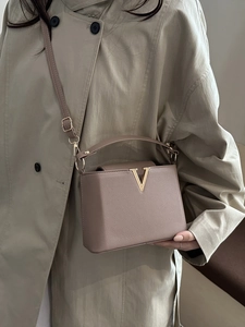 Sac à main élégant en cuir rose poudré avec boucle V dorée porté sur un trench-coat