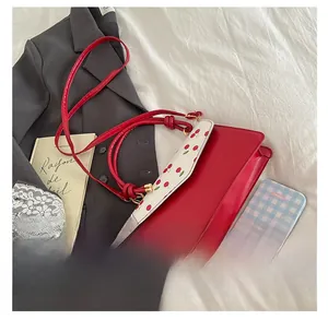 Detail view of red cherry print crossbody bag showing size comparison with small notebook