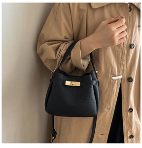 Detail of black litchi grain leather bucket bag with gold twist lock on trench coat
