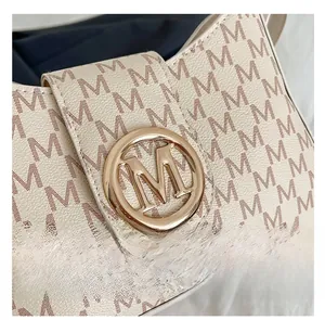 Detail of creamy white monogram leather bag with gold M-logo buckle on textured fabric
