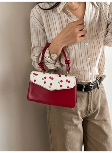 Detail of red and white cherry print handbag with golden hardware and leather texture