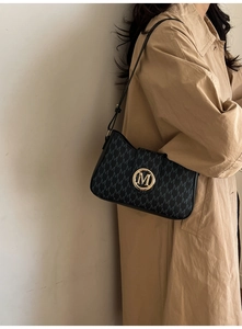 Close-up of black crossbody bag with gold M-logo and jacquard pattern on a trench coat
