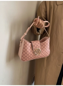 Détail d'un sac à bandoulière rose avec motif M et logo doré sur un trench-coat beige