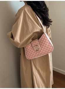Close-up of pink crossbody bag with M-pattern texture and gold metal buckle on model