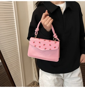 Detail of light pink strawberry print handbag with knotted handle and metal buckles