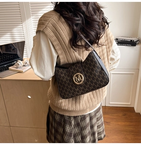 Macro detail of brown retro shoulder bag featuring golden M-logo clasp and letter prints