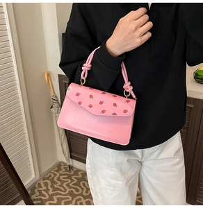 Close-up of pink handbag featuring red strawberry prints and a knotted rope handle detail