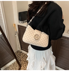 Model view of cream shoulder bag with M-pattern print and gold clasp for vintage look