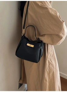 Modèle portant un sac seau noir en cuir à motif litchi avec fermoir doré tournant