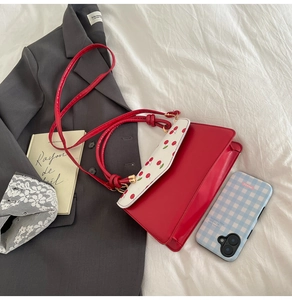 Détail du sac rouge avec imprimé cerise sur rabat blanc et ferrures en métal doré
