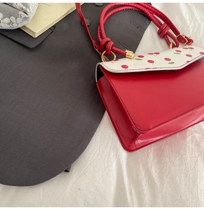 Détail du sac à main en cuir PU rouge avec rabat à motif cerise et accents dorés