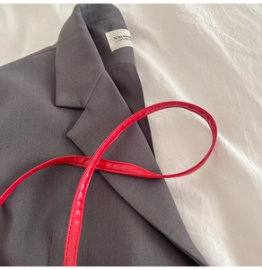 Détail de la bandoulière fine en cuir rouge vif posée sur une veste grise