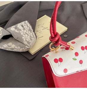 Détail de l'imprimé cerise sur sac à rabat avec bandoulière nouée et boucles dorées