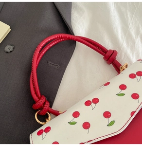 Vue détaillée de la poignée du sac rouge avec rabat imprimé cerise et boucles dorées