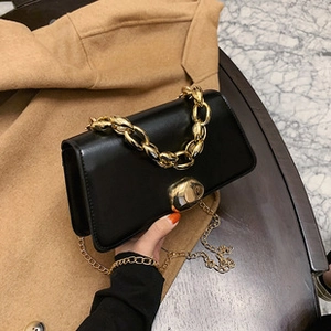 Detail of a black glossy crossbody bag featuring a gold pebble lock and chunky chain handle
