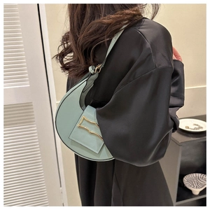 Detailed view of mint green crescent shoulder bag with wavy gold hardware and strap
