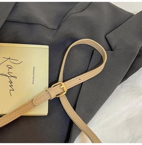 Détail d'une fine ceinture en cuir grainé beige avec boucle à ardillon dorée chic