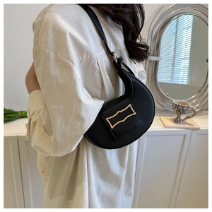 Detail of black faux leather crescent shoulder bag with golden geometric clasp on a model