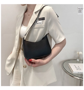 Minimalist black leather crescent-shaped underarm bag shown in a stylish home setting